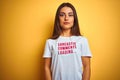 Beautiful woman wearing fanny t-shirt with irony comments over isolated yellow background with serious expression on face