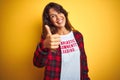 Beautiful woman wearing funny t-shirt with irony comments over isolated yellow background happy with big smile doing ok sign,