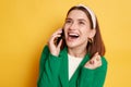 Beautiful woman wearing green jacket talking on mobile phone laughing hearing funny news expressing happiness posing isolated over