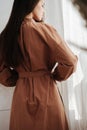 Beautiful woman in a brown dress standing next to a curtain. View from behind. Royalty Free Stock Photo