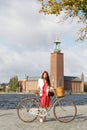 Beautiful woman wearing red dress dress holding a vintage bicycle in front of Stockholm City Hall Royalty Free Stock Photo