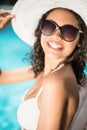 Beautiful woman wearing white bikini and hat sitting near pool Royalty Free Stock Photo