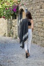 Beautiful woman wearing white loose pants, black crop top and sandals, walking with a gray shawl