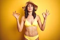 Beautiful woman wearing yellow bikini and summer hat over isolated yellow background relax and smiling with eyes closed doing Royalty Free Stock Photo