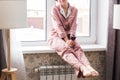 Beautiful woman wears pajamas with a glass of red wine sits on the windowsill near the beautiful window at home. Stay Royalty Free Stock Photo