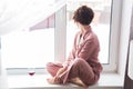 Beautiful woman wears pajamas with a glass of red wine sits on the windowsill near the beautiful window at home. Stay Royalty Free Stock Photo