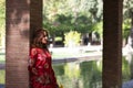 A beautiful woman wears a traditional Moroccan dress in red and embroidered in gold and silver. The beautiful woman is leaning on