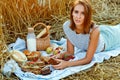 A beautiful woman in a wheat field on a picnic with food at sunset. A young woman is lying on a blanket against the background of