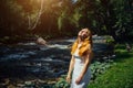 Beautiful woman in white dress with long red hair raised face to the sun on the bank of river in green summer forest.  Portrait of Royalty Free Stock Photo
