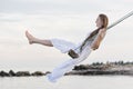 Beautiful woman in white dress rides a rope swing over water. Vacantion at the sea