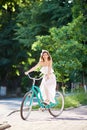 Beautiful woman in white dress riding vintage blue bike in a park. Royalty Free Stock Photo