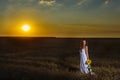 Woman In White Dress In A Wheat Field With A Sunflower Flower At Sunset