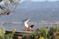 A beautiful woman in a white gymnastic jumpsuit is engaged in yoga on the background of the mountains and the sea Royalty Free Stock Photo