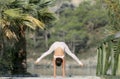 A woman in a white gymnastic jumpsuit is engaged in yoga on the background of water and a green mountain slope Royalty Free Stock Photo