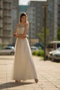 Beautiful woman in white long dress posing in the city