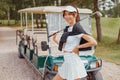 Beautiful woman in white outfit standing near golf cart Royalty Free Stock Photo