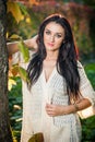 Beautiful woman in white posing in autumnal park. Young brunette woman spending time in autumn near a tree in forest