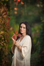 Beautiful woman in white posing in autumnal park. Young brunette woman spending time in autumn near a tree in forest