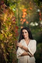 Beautiful woman in white posing in autumnal park. Young brunette woman spending time in autumn near a tree in forest