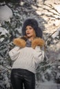 Beautiful woman in white pullover with over-sized fur cap enjoying the winter scenery in forest. Blonde girl posing Royalty Free Stock Photo