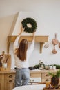 Beautiful woman in white sweater hanging a Christmas wreath on her kitchen. Royalty Free Stock Photo