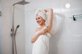 Beautiful woman in white towel shaving her armpits with razor in shower cabin. Depilatory procedure at bathroom