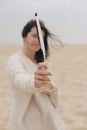 Beautiful woman with windy hair holding feather on background of sandy beach and sea, tranquil moment. Stylish young boho female