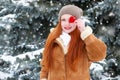 Beautiful woman on winter outdoor posing with heart shape toys, holiday concept, snowy fir trees in forest, long red hair, wearing Royalty Free Stock Photo