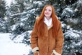 Beautiful woman on winter outdoor, snowy fir trees in forest, long red hair, wearing a sheepskin coat Royalty Free Stock Photo