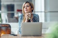 Beautiful woman working with laptop while drinking a cup of coffee looking forward in living room at home Royalty Free Stock Photo