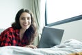 Beautiful woman working on a laptop with smiling and lying down on the bed at a condominium in the morning Royalty Free Stock Photo