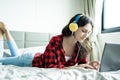 Beautiful woman working and listening to music on a laptop with yellow headphone and lying down on the bed at a condominium in the