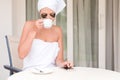 Beautiful woman wrapped in towel after shower with patches under eyes is drinking coffee and using her phone at the hotel terrace Royalty Free Stock Photo