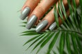 Beautiful woman's hand with gray manicure holds a palm leaf on a light background in a closeup view. French nail art Royalty Free Stock Photo