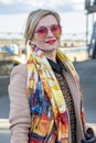 A beautiful WOMAN of 40-45 years old with glasses and a scarf on the background of urban multi-storey buildings. Royalty Free Stock Photo