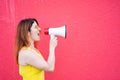 Beautiful woman in a yellow dress shouts in a megaphone on a red background. Stylish red-haired lady in sunglasses Royalty Free Stock Photo