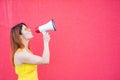 Beautiful woman in a yellow dress shouts in a megaphone on a red background. Stylish red-haired lady in sunglasses Royalty Free Stock Photo