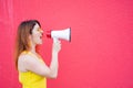 Beautiful woman in a yellow dress shouts in a megaphone on a red background. Stylish red-haired lady in sunglasses Royalty Free Stock Photo