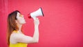 Beautiful woman in a yellow dress shouts in a megaphone on a red background. Stylish red-haired lady in sunglasses Royalty Free Stock Photo