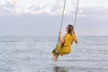 Beautiful woman in yellow dress sits on a rope swing over sea. Calm relax loneliness