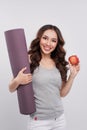 Beautiful woman with a yoga mat, hand holding red apple. Royalty Free Stock Photo