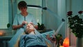 Beautiful woman getting facial massage with jade roller at beauty salon with dim light around