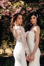 Beautiful women in luxurious wedding dresses with accessories posing in garden with blossoming sakura trees