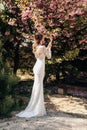 Beautiful women in luxurious wedding dresses with accessories posing in garden with blossoming sakura trees