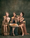 Pretty women in vintage 20s dresses. Young girls in art action sitting together and posing on wall background.