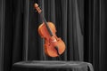 Beautiful wooden cello on table covered with black satin fabric against background of black curtain. 3d rendering