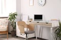 Beautiful workplace with laptop on wooden table, chair and decor elements in room