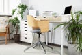 Beautiful workplace with laptop on white wooden table, chair and houseplants in room