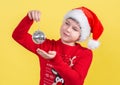 A beautiful 10-year-old boy in a Santa Claus hat holds a Christmas disco ball on a yellow background. Isolate. Royalty Free Stock Photo