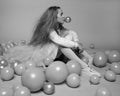 A beautiful 10-year-old girl with long fluffy hair in fashionable clothes sits in the Studio among balloons and inflates a bubble Royalty Free Stock Photo